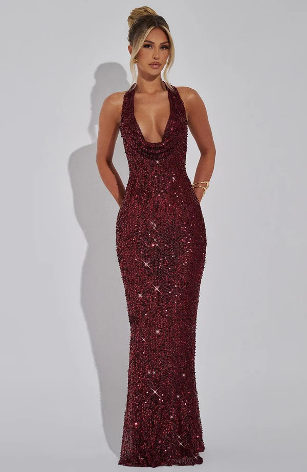 A woman modeling a floor-length, deep V-neck evening gown covered in shimmering dark burgundy sequins against a light gray studio background.