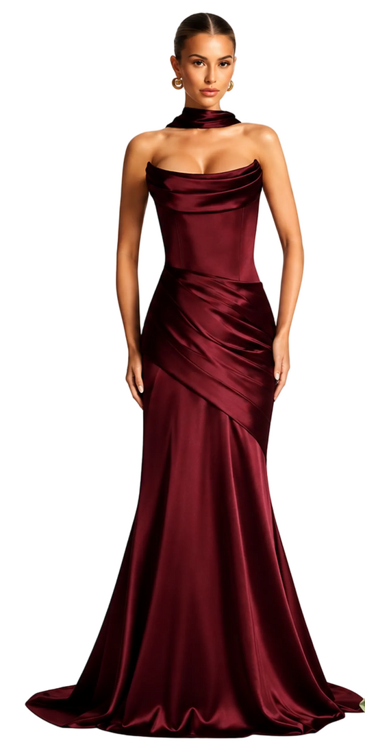 A woman modeling a floor-length burgundy satin gown with a draped, wrap-style skirt and a matching choker collar, set against a plain white background.