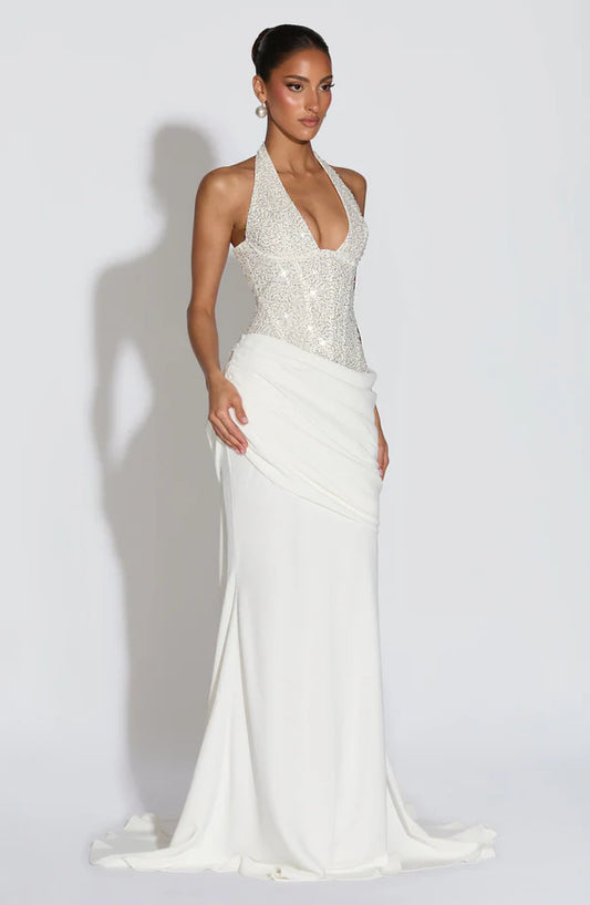 Woman wearing a white evening gown with a halter neck design on a plain background